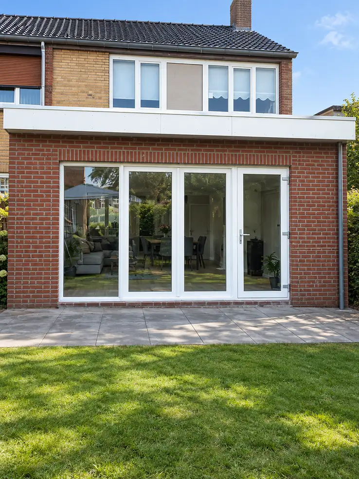Bakstenen aanbouw met plat dak en een brede glazen pui naar de tuin.