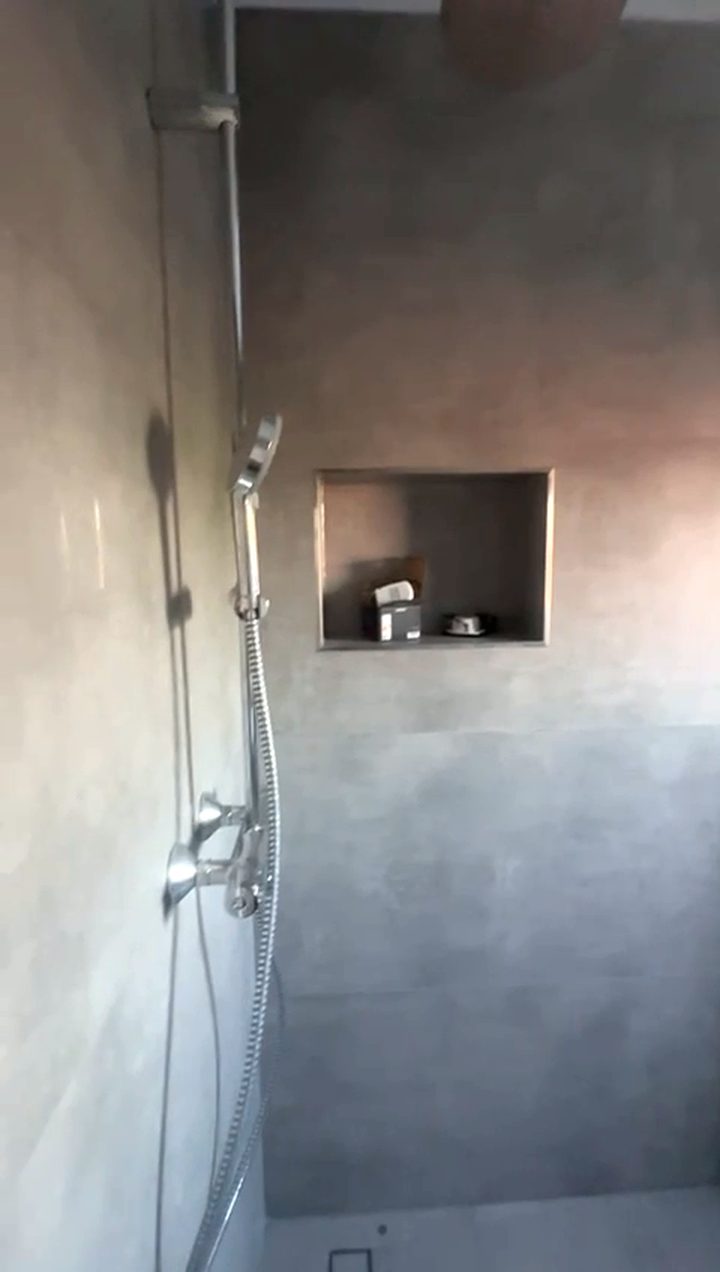 Afgewerkte badkamer: douchehoek met gladgestuukte grijze wanden, een inbouwnis en een chromen doucheset aan een glijstang.