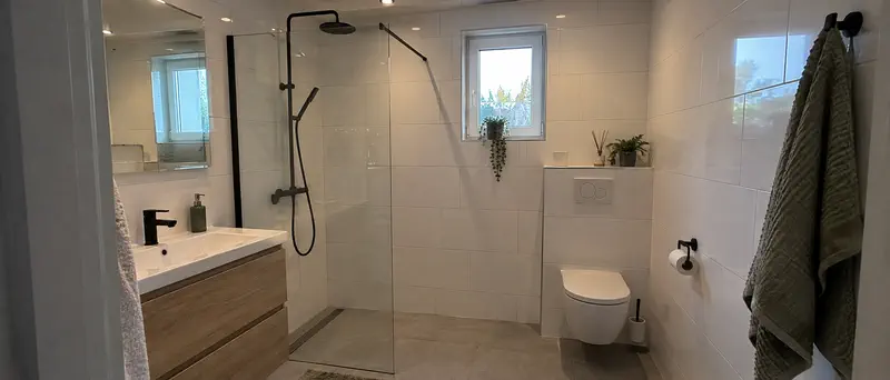 Sfeerbeeld: lichte badkamer met inloopdouche, witte wandtegels, grijze vloertegels en een zwevend toilet.