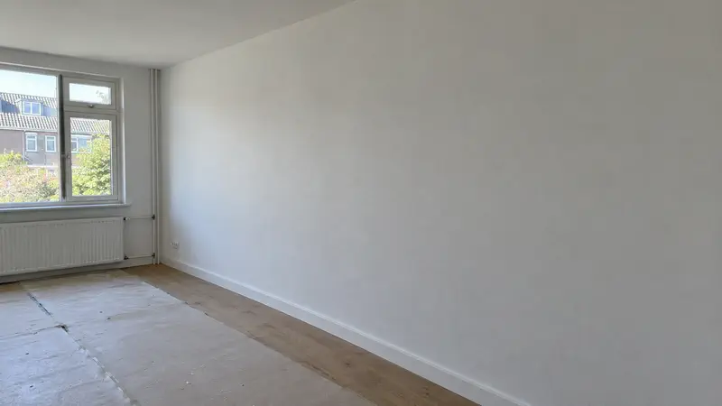 Sfeerbeeld: lege kamer met glad gestuukte, droge wanden en een deels afgedekte houten vloer