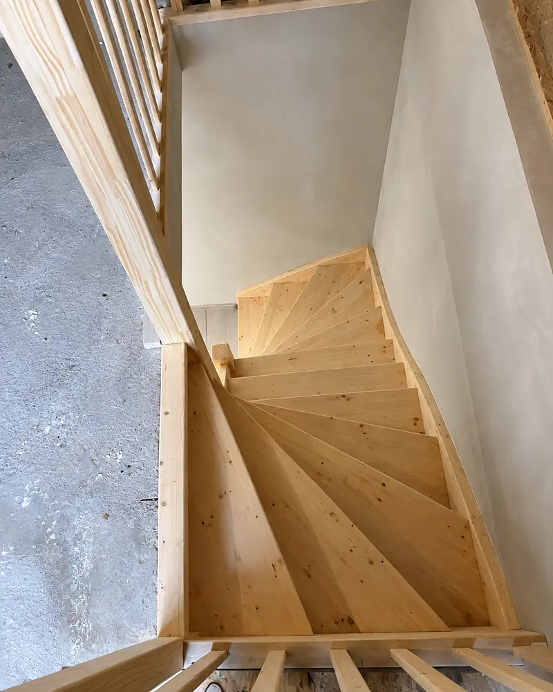 Nieuwe houten dubbele kwartslagtrap van bovenaf gezien, in een pas gestuukt trappenhuis.