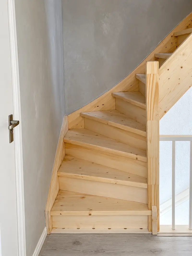 Trappenhuis met vers grijs stucwerk op de wanden en een nieuwe houten trap.